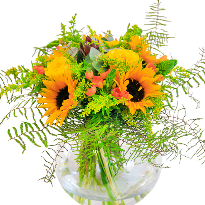 The first glimpse of this cheerful bouquet conjures the warmth of a sun-drenched walk along the Millbank riverside. Towering sunflowers with deep brown centers radiate golden brilliance, illuminating the arrangement in much the same way morning light plays off the water. At their side, plush yellow garden roses spiral open, their citrusy tones and sweet scent adding a classic, refined touch. Bright red Hypericum berries are scattered like jewel-toned confetti amidst the verdant foliage-a nod to the creativity that defines Millbank and its galleries. Wispy green fern fronds and pale golden filler greens cascade with carefree abandon, softened by subtle hints of silvery eucalyptus. Presented in a clear, round glass vase, the fresh stems rest visibly in water, giving the arrangement a sense of airy transparency and contemporary elegance. Ideal as a gift for birthdays, anniversaries, or acts of gratitude, this bouquet brings the essence of Millbank's seasonal beauty indoors, crafted with care by attentive local florists who know every twist along the Thames.