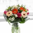Overflowing with radiant energy, this Millbank-inspired bouquet offers a kaleidoscope of rich hues and lush textures, expertly arranged for contemporary elegance. Dominant orange and peach gerberas stand tall with luminous, soft petals, their earthy brown centres radiating warmth and joy like a gathering at nearby Riverside Gardens. Luxurious magenta roses spiral discreetly among them, lending a tone of romance, while clusters of snowy alstroemeria and miniature white blooms infuse the display with purity and gentle contrast. Blush-pink touches and tiny sprays of white filler flowers create layers of visual abundance, each detail reminiscent of Millbank's vibrant weekend atmosphere. The base is gracefully encompassed by broad, glossy aspidistra leaves that curve protectively, their robust green surfaces framing the bounty above. Sprigs of slender, pointed foliage weave throughout, imbuing the bouquet with a wild, exuberant freshness. Standing in a clear glass vase, the visible stems ground the arrangement with an organic authenticity-much like the riverside stretches that define the local landscape. Gentle, diffused sunlight illuminates every detail, ensuring the bouquet remains the vibrant, joyful centerpiece. Perfect as a gift for birthdays, professional milestones or simply to brighten a Millbank home, this bouquet brims with the floral excellence and heartfelt artistry that distinguish Millbank's florists.